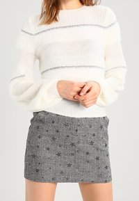 Vit stickad tröja med texturerade ränder och silverdetaljer, som är kombinerad med en rutmönstrad svart och grå kjol med blommönster.