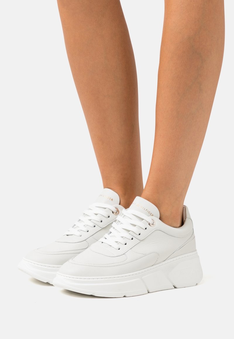 Sneakers bianchi realizzati in pelle testurizzata con una suola spessa e a piattaforma. Le caratteristiche includono un design con lacci e dettagli metallici sugli occhielli.