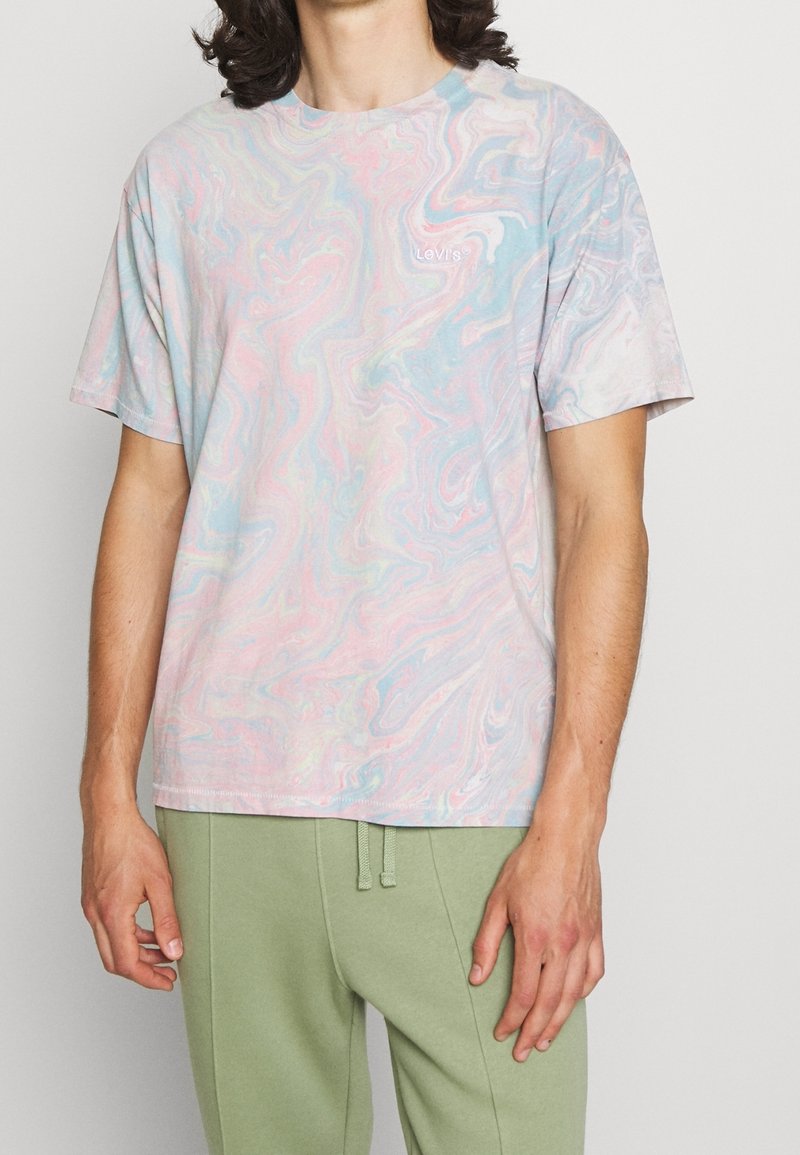 T-shirt à manches courtes dans un motif marbré pastel avec des couleurs rose clair, bleu et blanc, comportant un petit logo de marque sur la poitrine.