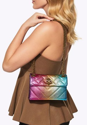 Donna che tiene una borsa in pelle trapuntata color arcobaleno con tracolla a catena dorata sulla spalla, indossa un top marrone senza maniche.