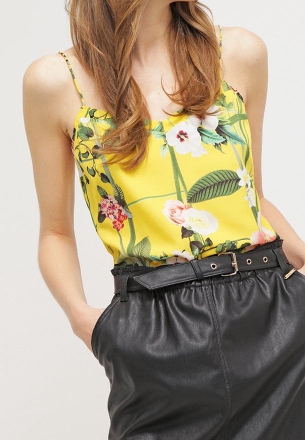 Floral print camisole in yellow satin with thin straps, paired with high-waisted black faux leather trousers featuring a belt.