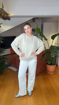 Beiges übergroßes Sweatshirt mit überschnittenen Schultern, kombiniert mit weißen, weit geschnittenen Hosen. Silberne Sneakers vervollständigen den lässigen Look.