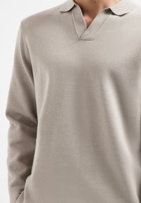 Lichtgrijze pullover van zachte, textuurstof. Heeft een V-hals en een korte, ronde kraag. Lange mouwen met een relaxte pasvorm.
