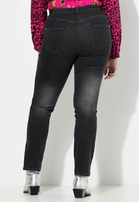 Los jeans de mezclilla negros tienen un diseño ajustado con una cintura de altura media y dos bolsillos traseros. Se llevan con botas de tobillo plateadas y brillantes.