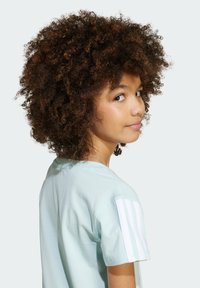 Light blue cotton t-shirt with a relaxed fit, featuring white striped accents on the sleeves. Curly hair frames the side profile of the model.
