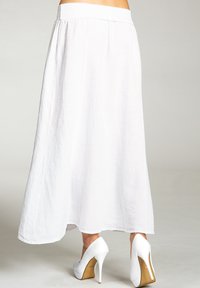 Langer weißer Rock aus leichtem Stoff mit fließendem Design. Verfügt über einen breiten Taillenbund und einen ungesäumten Saum. Kombiniert mit weißen High Heels.