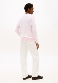 Svetlo roza majica z dolgimi rokavi iz mehke tkanine, z okroglim izrezom in rebrastimi manšetami. Kombinirana z belimi hlačami s pravo nogo in črnimi čevlji.