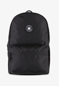 Sac à dos en tissu noir avec le haut arrondi, poche zippée à l'avant et patch circulaire arborant un logo étoilé. Surface texturée, design minimaliste.
