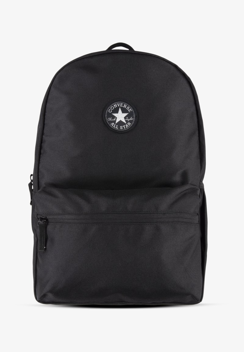 Sac à dos en tissu noir avec le haut arrondi, poche zippée à l'avant et patch circulaire arborant un logo étoilé. Surface texturée, design minimaliste.
