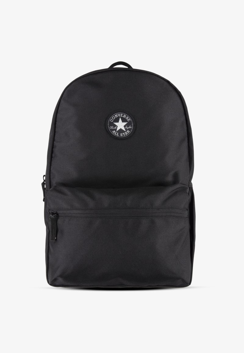 Sac à dos en tissu noir avec le haut arrondi, poche zippée à l'avant et patch circulaire arborant un logo étoilé. Surface texturée, design minimaliste.