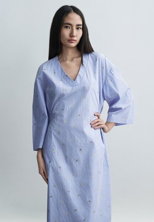 Modré a biele pruhované šaty s výstrihom do V, nadmernými rukávmi a žltými vyšívanými akcentmi, vyrobené z hladkej, ľahkej látky.