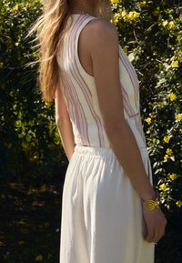 Top senza maniche con righe verticali rosa e bianche, abbinato a una gonna bianca, fluida, con vita elasticizzata; polso della modella adornato con un braccialetto d'oro.