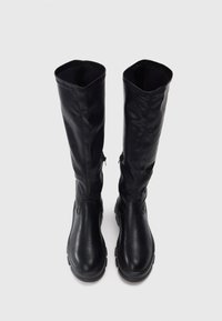 Knee-high melni ādas zābaki ar gludu tekstūru, noapaļotiem pirkstiem un masīvu zoli. Ir slīpās šuves augšējā pusē.