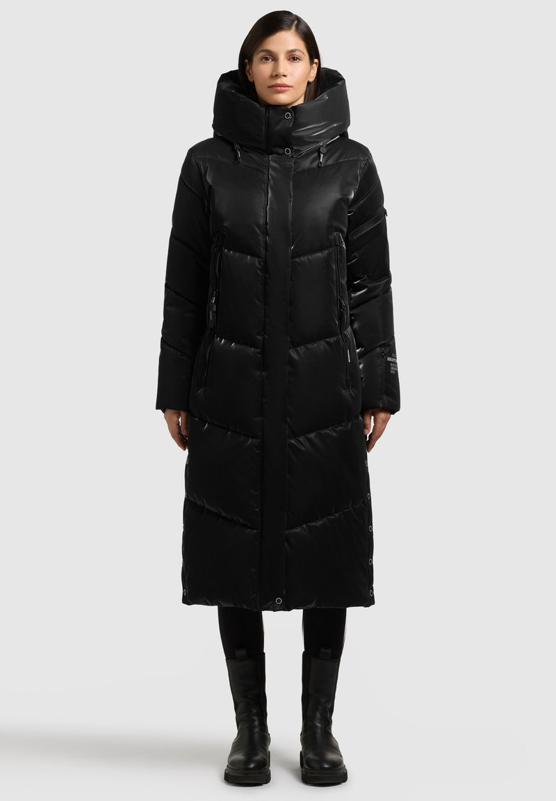 Zwarte gewatteerde jas met hoge kraag, voorzien van een doorgestikt ontwerp, ritszakken en drukknopen, tot halverwege de kuit.