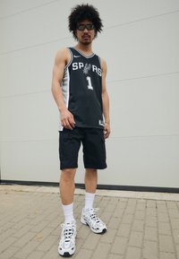 Juodas krepšinio marškinėlis su baltomis detalėmis, su skaičiumi "1" ir užrašu "SPURS". Suderintas su juodomis šortais ir baltais sportiniais bateliais.
