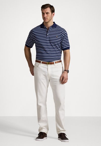 Cămașă polo cu dungi bleumarin și alb, cu guler, asortată cu pantaloni de culoare crem și curea din piele maro, completată cu adidași maro.