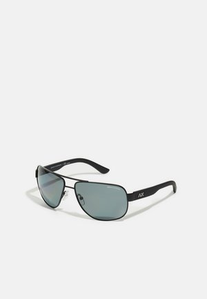 Lunettes de soleil en métal noir avec verres teintés gris, design courbé, coques de nez ajustables et logo sur le côté des branches sombres.