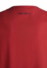 Czerwona koszulka z krótkim rękawem wykonana z bawełny, z okrągłym dekoltem i prostym wzornictwem, z napisem "PEPE JEANS" w kolorze czarnym z tyłu.