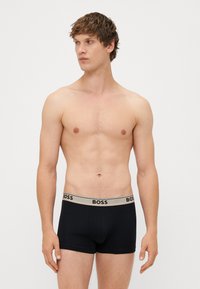 Boxeri negri din bumbac cu un brâu elastic bej, având numele brandului "BOSS" în negru. Material neted, design ajustat.