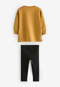 Mosterdgele sweatshirt met een ronde hals en ribgebreide boorden, gecombineerd met zwarte aansluitende leggings. Zachte stof, eenvoudig ontwerp, geen patronen.