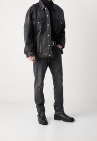 Chaqueta vaquera negra con botones a presión, combinada con vaqueros gris oscuro y botas negras de cuero hasta el tobillo. Diseño sencillo, ajuste relajado y tela resistente.