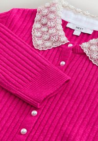 Cardigan côtelé rose vif avec boutons en perle et col en dentelle orné de grappes de petites perles blanches.