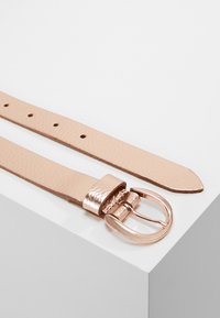 Beige leather belt with a textured finish, featuring a metallic rose gold buckle, five holes for adjustment, and a smooth tapering end.