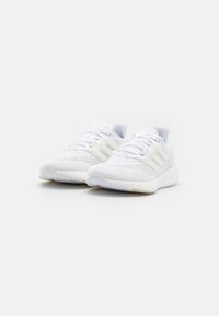 White athletic shoes made of breathable mesh and synthetic materials, featuring a textured sole, lace closure, and three stripe design accents.