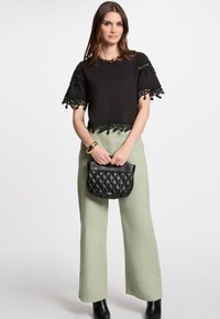 Sort top med blonderkant, grønne vide bukser og en quilted sort handbag. Funktioner inkluderer korte ærmer og glatte stofstrukturer.
