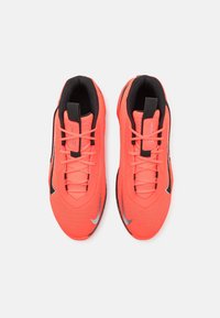 Paire de chaussures de sport orange vif avec des accents noirs et argentés, une doublure intérieure noire et des lacets orange assortis vus de dessus.