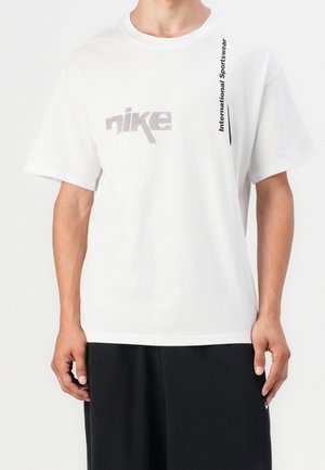 Biała bawełniana koszulka z szarym kropkowanym logo "Nike" na klatce piersiowej oraz czarnym pionowym napisem "International Sportswear" wzdłuż boku.
