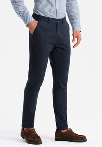 Pantaloni blu navy realizzati in tessuto liscio, slim fit, con tasche laterali, chiusura a bottone, abbinati a scarpe in suede marroni.