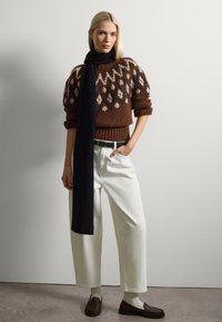 Suéter de punto marrón con un yugo estampado, combinado con pantalones de pierna ancha blancos, una bufanda negra y mocasines oscuros. Texturas suaves.