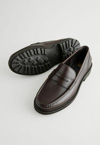 Mocasines de cuero marrón con un diseño cosido, suela de goma plana con patrones de tracción y una banda decorativa en la parte superior.