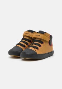 Zapatos de cuero marrón de caña alta con punteras de goma negra y acentos de malla gris. Presentan cordones negros y una correa de velcro para el cierre. Logotipo de Geox visible.