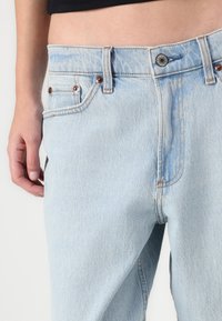 Light blue denim jeans with a classic five-pocket design, copper rivets, and visible stitching along the seams. Textured fabric.