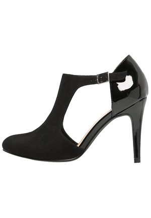 Chaussure à talons hauts noirs avec une tige en daim, un design découpé et un talon en cuir verni. Bride de cheville réglable avec une boucle métallique en accent.