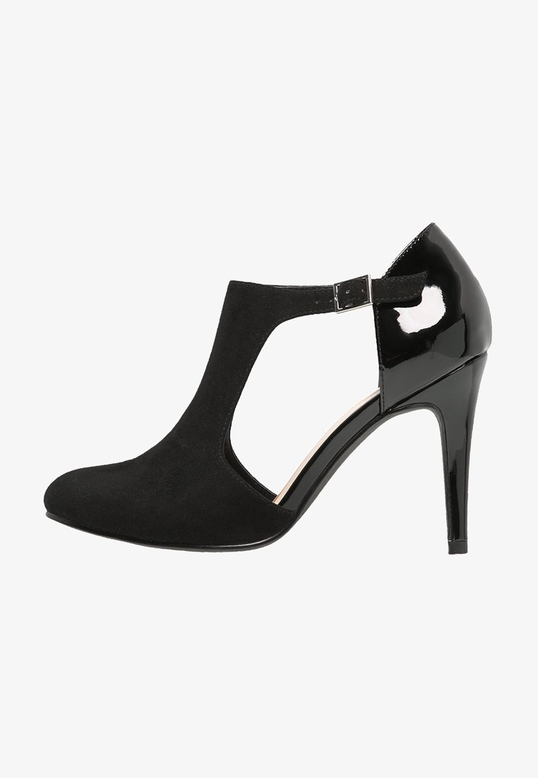 Chaussure à talons hauts noirs avec une tige en daim, un design découpé et un talon en cuir verni. Bride de cheville réglable avec une boucle métallique en accent.