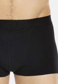 Schwarze Boxer-Briefs aus weichem Stoff mit einem breiten, strukturierten Bund, der ein dezentes Logo trägt. Das Design umfasst eine Vordernaht zur Formgebung.