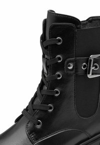 Bottines en cuir noir à lacets, avec œillets en métal, panneau latéral élastique et détail de sangle à boucle argentée.