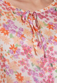 Květinová blůza na pastelovém pozadí, zdobená oranžovými, růžovými a fialovými květinami. Lehčí materiál, kulatý výstřih s detailem na zavázání.