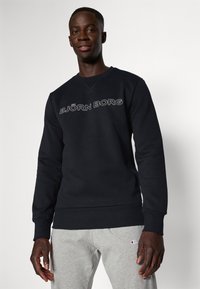 Μαύρη μπλούζα φτιαγμένη από μείγμα βαμβακιού, με στρογγυλή λαιμόκοψη και ριμπ μανσέτες, με λευκή επιγραφή "BJÖRN BORG" στο στήθος.