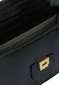 Borsa a mano in pelle nera con stampa a forma di coccodrillo, con chiusura in tonalità oro, dotata di un compartimento con zip e fodera interna liscia.