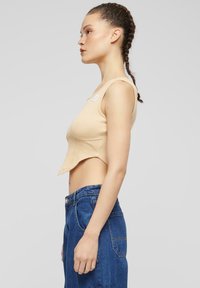 Top corto de canalé beige con cuello redondo y detalles de costura en la costura lateral, combinado con unos vaqueros de denim azul de tiro alto con cierre de botón.