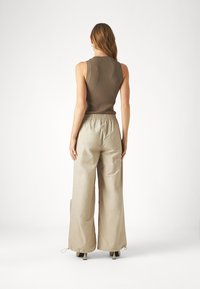 Gestreift braunes Tanktop und hellbeige, weit geschnittene Hose mit elastischem Bund und Kordelzug. Glatte Textur, knöchellang, minimalistisches Design.