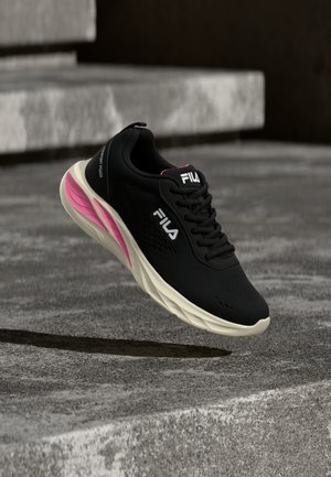 Fekete FILA tornacipő fehér talppal és rózsaszín részlettel, lebegve betonlépcsők felett, bemutatva a cipő oldalnézetét és felülnézetét.