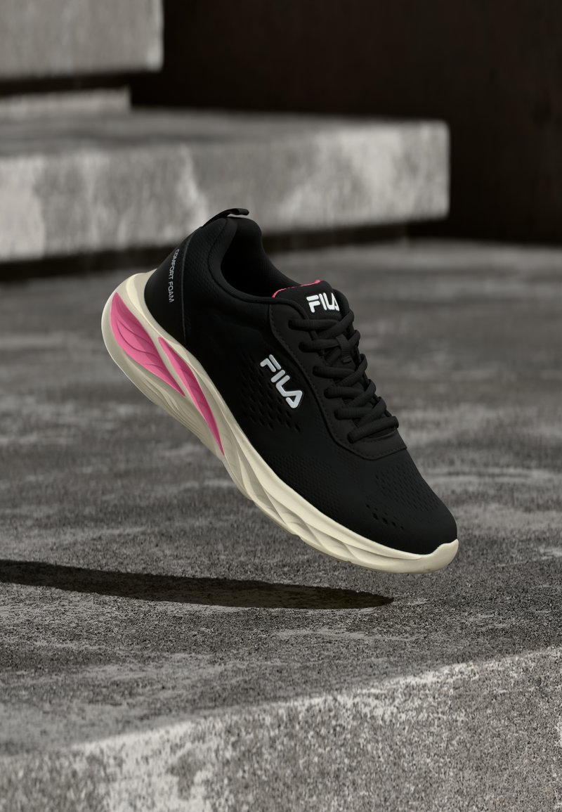 Baskets noires FILA avec une semelle blanche et un accent rose flottant au-dessus d'escaliers en béton, présentant des vues latérales et supérieures de la chaussure.