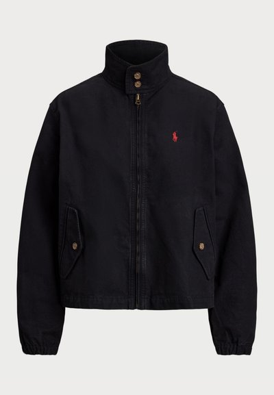 Fekete dzseki magas gallérral, cipzáras záródással és két oldalsó zsebbel. A bal mellen vörös logóval rendelkezik és rugalmas mandzsettákkal van ellátva. Pamut anyag.