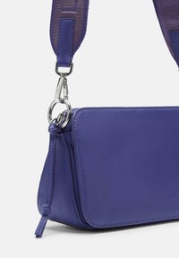 Borsa a tracolla viola in pelle con ampia tracolla in tessuto regolabile e chiusura in metallo argentato su sfondo bianco.