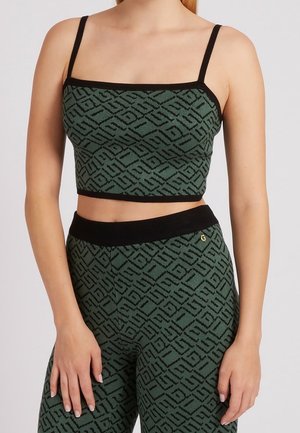 Femme portant un crop top à motifs verts et un pantalon taille haute assorti avec des bordures noires et de fines bretelles noires.